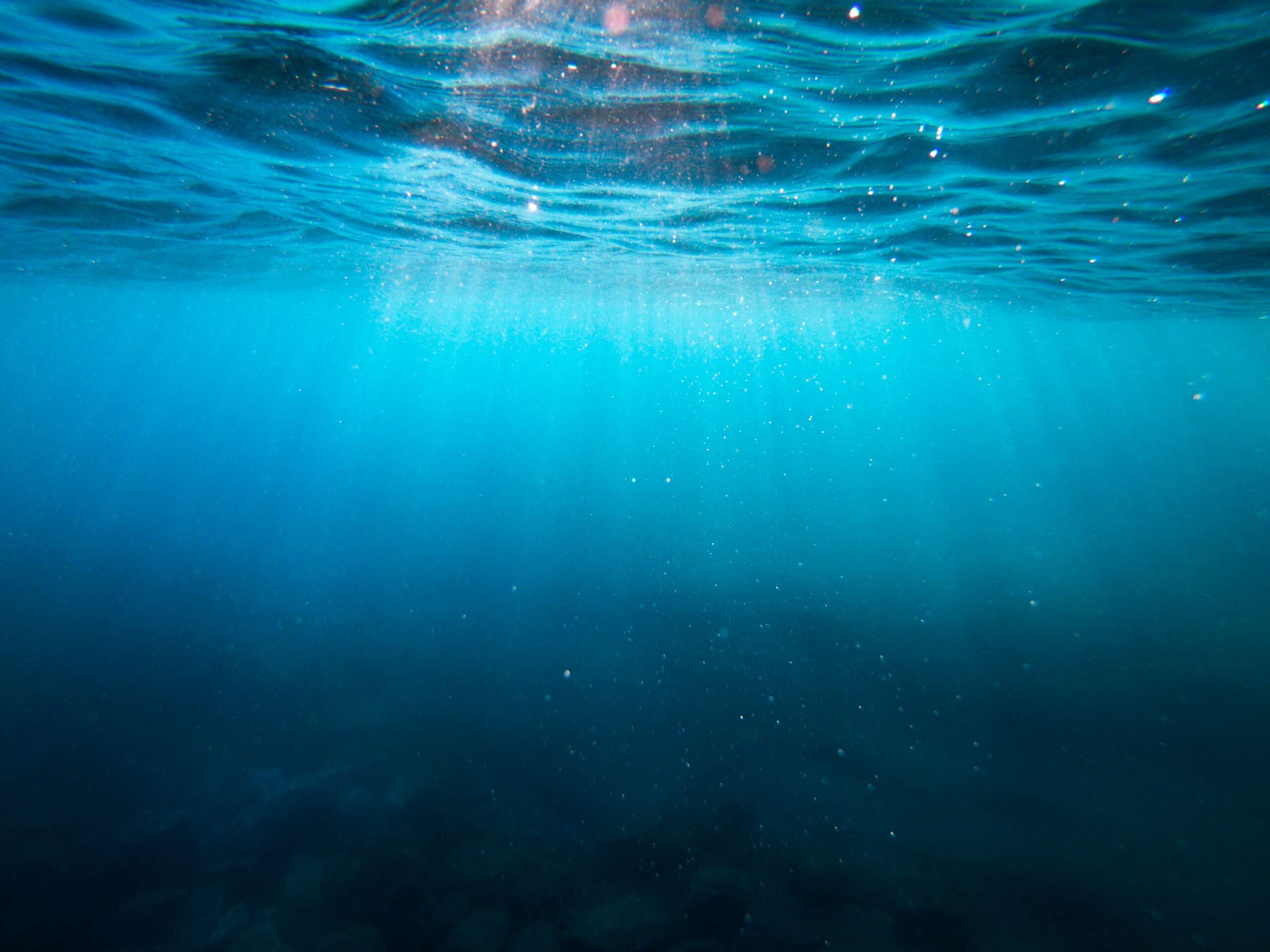 Looking up through deep water to the sun shining through the water surface.